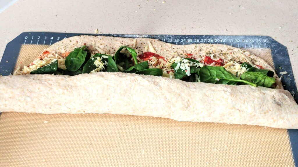 Vegetarian pizza scrolls on a baking tray topped with spinach, cheese and a tomato paste base partly rolled up - The Simple Healthy Hub