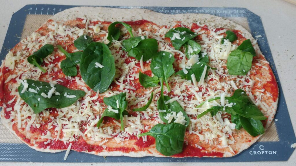Vegetarian pizza scrolls on a baking tray topped with spinach, cheese and a tomato paste base - The Simple Healthy Hub